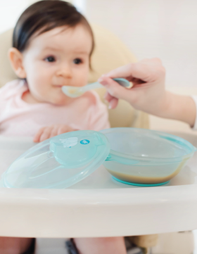 Beba sedi u stolici za hranjenje dok je majka hrani silikonskom kašičicom i kašicom iz Elfi činije
